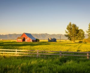 Summer sunset with a red barn and silos in rural Montana with Rocky Mountains in the background.