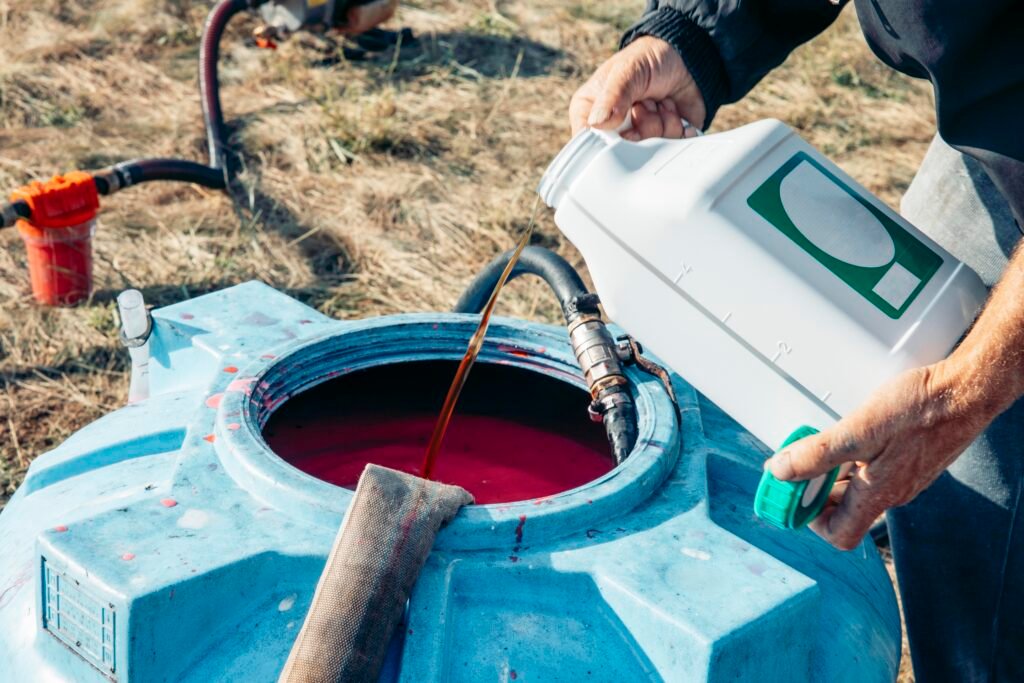 men's hands pouring a chemical into a large blue plastic tank filled, agricultural mixing process, hoses connected for chemical transfer in sunny rural field, agriculture, irrigation, chemistry, fungicides
